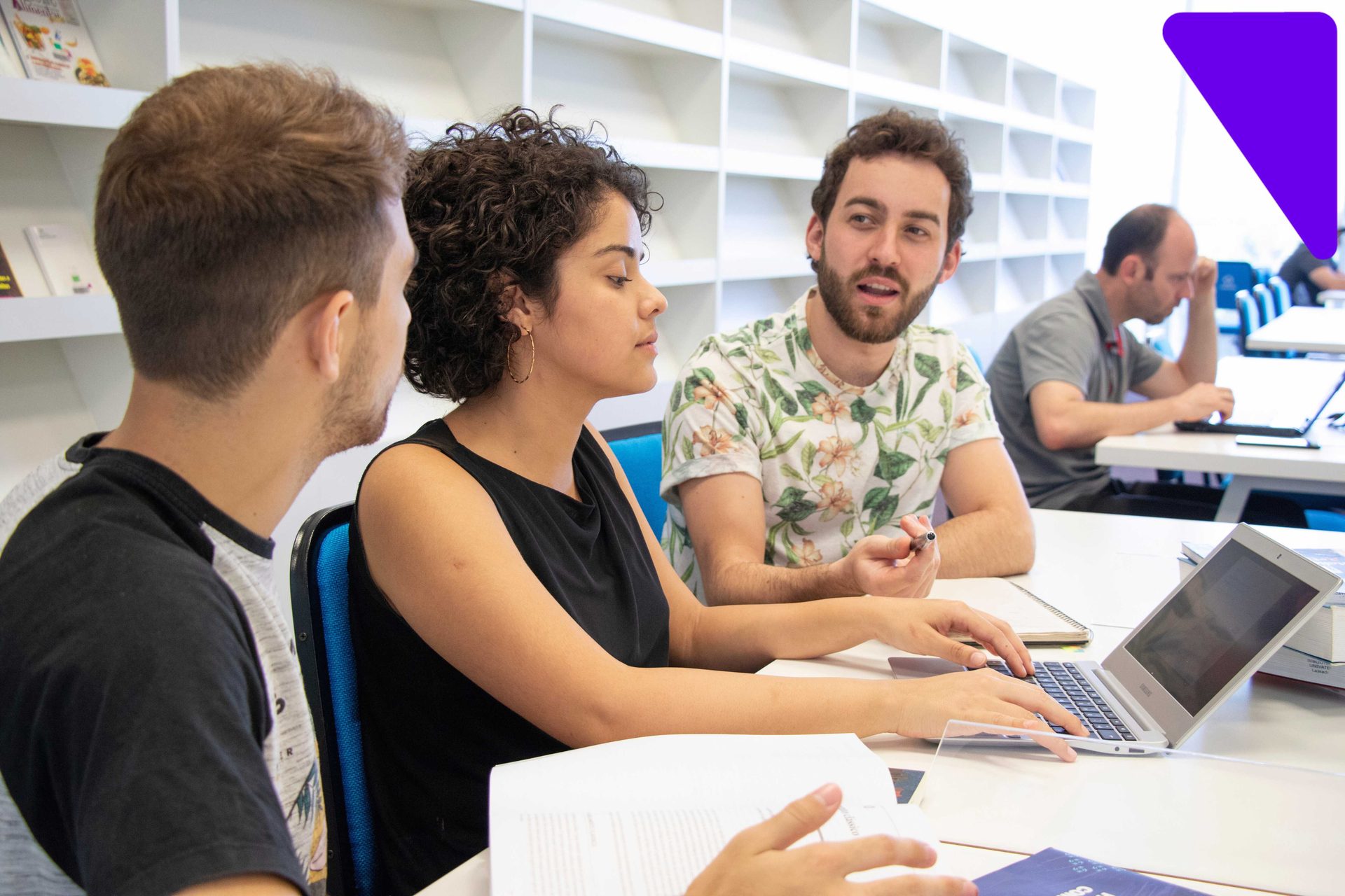 Três estudantes adultos reunidos em uma mesa de estudos com notebook em ambiente acadêmico, conversando e trocando experiências durante as aulas de pós-graduação em Administração na Univates.
